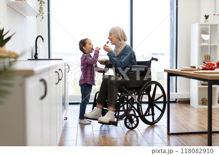 Muslim mother in wheelchair and daughter enjoy fresh salad together in kitchen 118082910