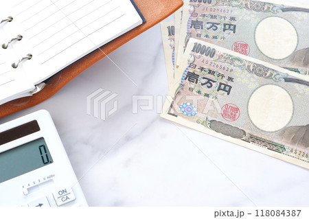 机の上に開いておかれたリング式のシステム手帳、電卓、福沢諭吉の肖像の一万円札紙幣 118084387