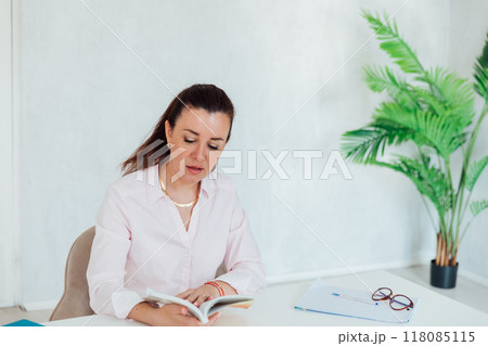 Beautiful business woman reading a book at her desk in the office Beautiful business woman reading a book at her desk in the office 118085115