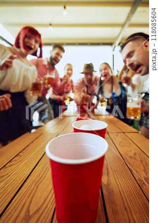 Group of people cheerfully playing beer pong, having fun and bar while celebrating beer festival. Bavarian traditions Group of people cheerfully playing beer pong, having fun and bar while celebrating beer festival. Bavarian traditions 118085604