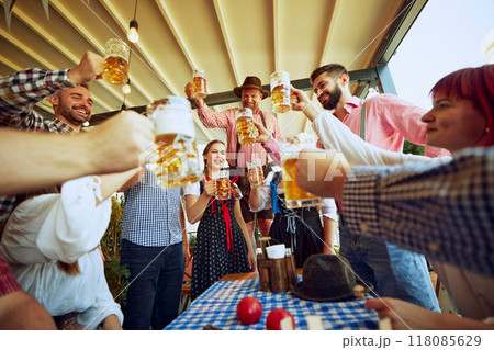 Men in traditional Bavarian clothes cheering group of his friends, people meeting at local pub for beer festival celebration 118085629