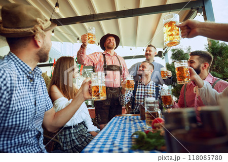 Group of friends, cheerful men and women raising beer mug in celebratory toast, having fun, leisure and enjoyment 118085780