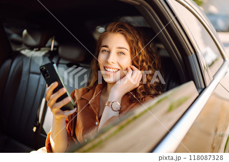 Smiling woman using smartphone while sitting in the back seat of a car. Business, technology concept 118087328