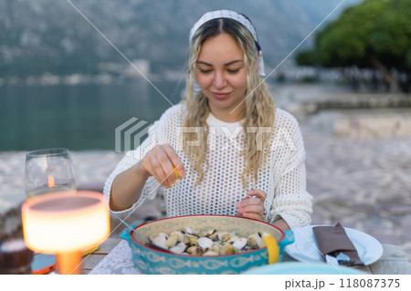 A woman eats mussels, a traditional Montenegrin dish, while sitting on the terrace of a restaurant near the Bay of Kotor. Seafood and good summer vacation concept 118087375
