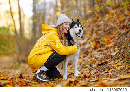 Beautiful young woman in a yellow coat walks in an autumn park with her pet husky. 118087636