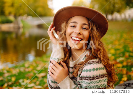 Happy woman in stylish sweater and hat outdoors in autumn park on plaid. Woman enjoys autumn nature. Happy woman in stylish sweater and hat outdoors in autumn park on plaid. Woman enjoys autumn nature. 118087836