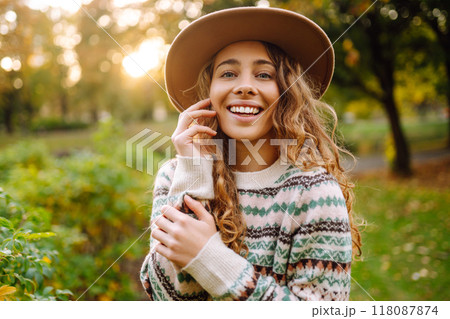 Happy woman in stylish sweater and hat outdoors in autumn park on plaid. Woman enjoys autumn nature. 118087874
