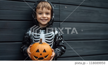 Smiling boy wearing skeleton costume holding jack-o'-lantern for halloween 118089950