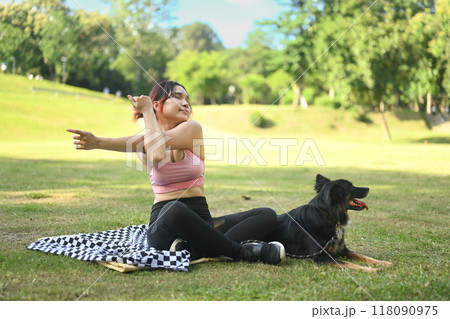 Young woman stretching her arms and resting after workout on a blanket in a park with her dog Young woman stretching her arms and resting after workout on a blanket in a park with her dog 118090975