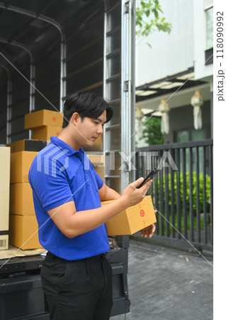 Young man courier holding cardboard box and using smartphone to confirm or manage deliveries Young man courier holding cardboard box and using smartphone to confirm or manage deliveries 118090992