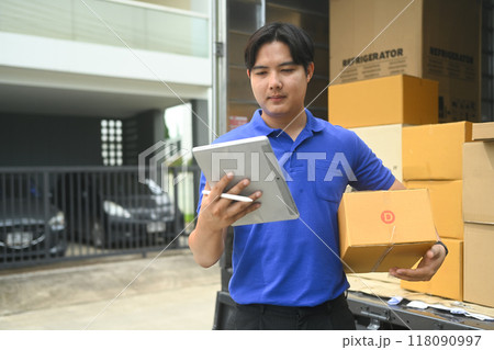 Delivery man holding cardboard box and using mobile phone beside an open truck filled with packages 118090997