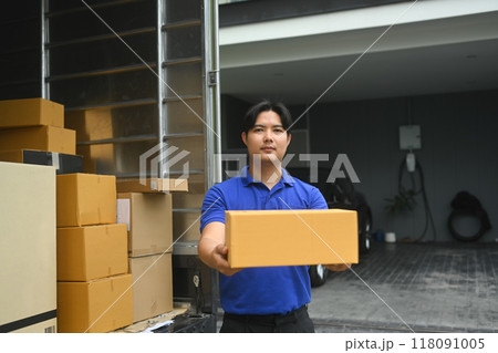 Portrait of delivery man holding cardboard box standing next to a truck filled with packages Portrait of delivery man holding cardboard box standing next to a truck filled with packages 118091005