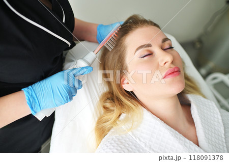 A dermatologist trichologist performs the procedure with a darsonval device to improve the condition and quality of the patient's hair. 118091378