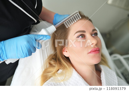 A dermatologist trichologist performs the procedure with a darsonval device to improve the condition and quality of the patient's hair. A dermatologist trichologist performs the procedure with a darsonval device to improve the condition and quality of the patient's hair. 118091379
