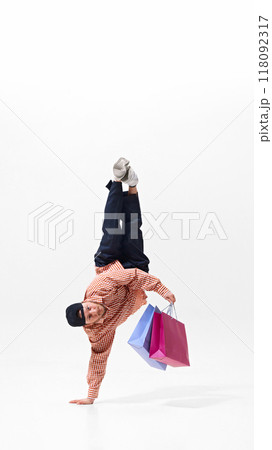 Dynamic image of young man in casual clothes doing one-handed handstand in breakdance pose with colorful shopping bags 118092317