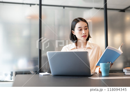 本を参考にしながらパソコンを使用して作業をしている女性 本を参考にしながらパソコンを使用して作業をしている女性 118094345