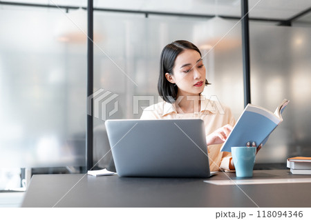 本を参考にしながらパソコンを使用して作業をしている女性 118094346