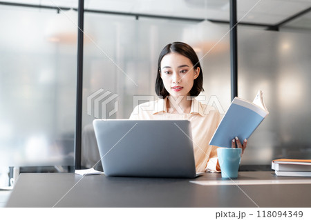本を参考にしながらパソコンを使用して作業をしている女性 118094349