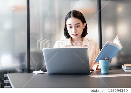 本を参考にしながらパソコンを使用して作業をしている女性 118094350