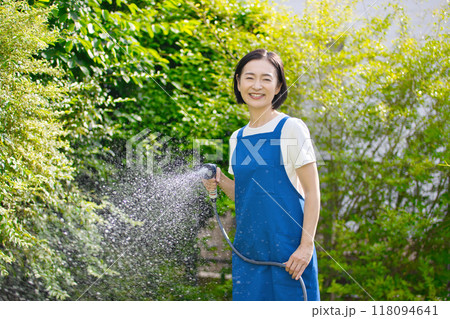庭の緑に水やりをする笑顔のミドル女性 118094641