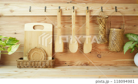 wooden spatula and spoon in different size hanging on wooden wall with wooden basket and chopping board on wooden counter 118094981