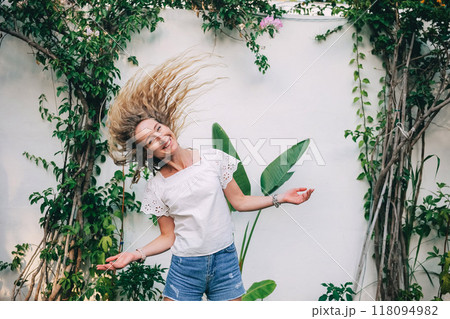 Young woman with flowing hair enjoying a sunny day in a lush garden with green plants 118094982