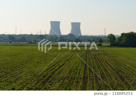 Vast green fields stretch towards majestic cooling towers under a clear blue sky, blending nature and industry in harmony Vast green fields stretch towards majestic cooling towers under a clear blue sky, blending nature and industry in harmony 118095253