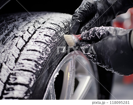 Mechanic wearing orange overalls inspecting car tire after washing 118095281