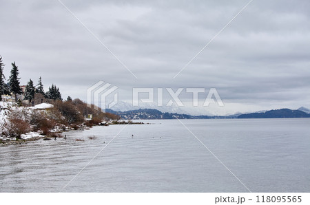 Scenic view of city buildings and a winter lake with snow-capped mountains in the background Scenic view of city buildings and a winter lake with snow-capped mountains in the background 118095565