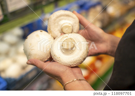Hands hold large champignons against the background of a blurred store window. Hands hold large champignons against the background of a blurred store window. 118097701