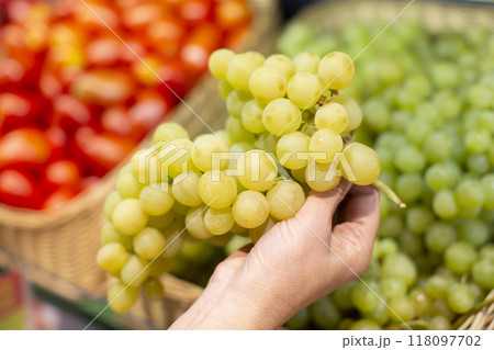 Hands hold a bunch of green grapes against the background of a blurred store counter. 118097702