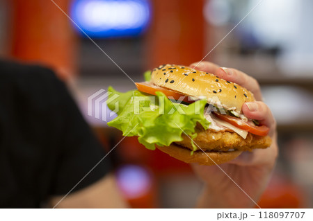 Hands holding a hamburger sprinkled with sesame seeds on a blurred background. 118097707