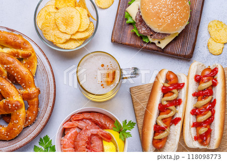 A vibrant photo showcasing a glass of beer surrounded by various snacks and fast food A vibrant photo showcasing a glass of beer surrounded by various snacks and fast food 118098773