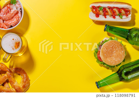 A vibrant photo showcasing a glass of beer surrounded by various snacks and fast food 118098791
