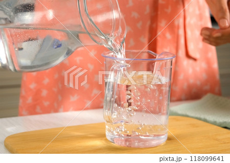 Woman pouring 500 ml of water in measure decanter to cook dish, hands close-up. 118099641