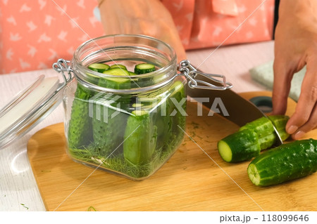 Woman cutting putting cucumbers in glass jar to cook pickles, hands close-up. Woman cutting putting cucumbers in glass jar to cook pickles, hands close-up. 118099646