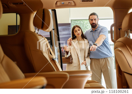 Shot from car cabin with beige leather interior of adult woman and man deciding on buying new car ,discussing passenger compartment design of demo model displayed at dealership center Shot from car cabin with beige leather interior of adult woman and man deciding on buying new car ,discussing passenger compartment design of demo model displayed at dealership center 118100261