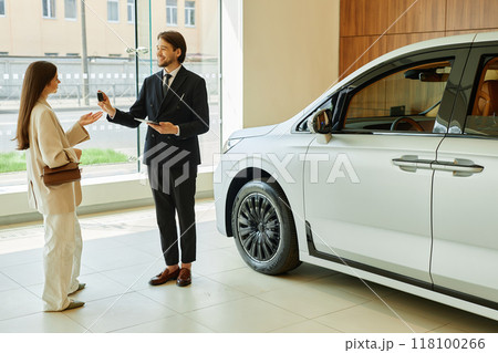 Full shot of smiling auto dealer handing key of new vehicle to female customer after successful car buying next to new automobile at dealership center Full shot of smiling auto dealer handing key of new vehicle to female customer after successful car buying next to new automobile at dealership center 118100266