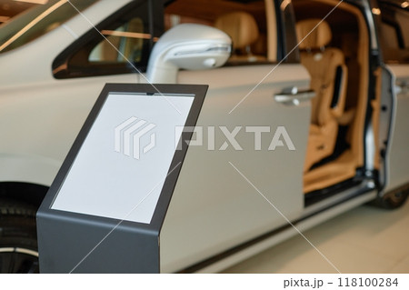 Car dealership information stand with blank mockup sheet displaying vehicle specifications in showroom, copy space 118100284