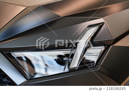 Close up on headlight of modern SUV automobile in futuristic design. Gray demo vehicle with matte coat displayed in car showroom at dealership center 118100285