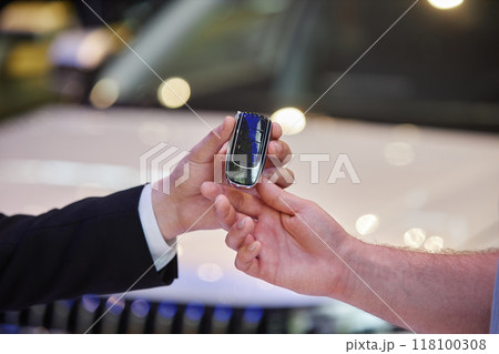 Close up on auto dealers hand giving smart key of new vehicle to male buyer at car dealership center, copy space 118100308