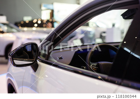 Side view mirror of shiny white car with opened window displayed in showroom at dealership center 118100344