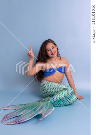 A happy pretty girl in a mermaid costume sits on a blue background 118101016