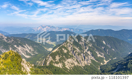 A breathtaking view of the Julian Alps in Slovenia showcases majestic peaks and lush valleys. The vibrant landscape is framed by a brilliant blue sky with scattered clouds. 118101397