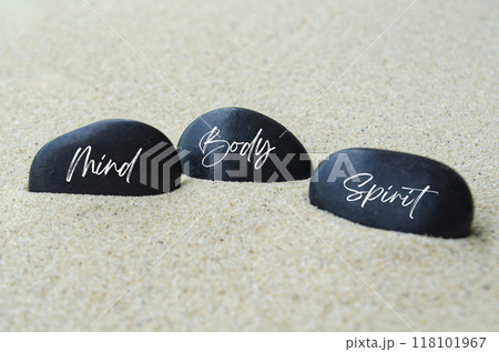 Mind, Body and Spirit text on black zen stones buried in the sand. Mind, Body and Spirit text on black zen stones buried in the sand. 118101967