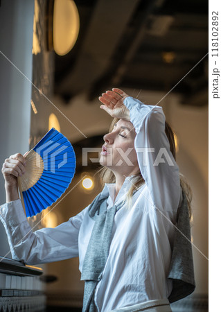 Woman suffering from heat stuffy air in office without air conditioning fanned herself with hand fan 118102892