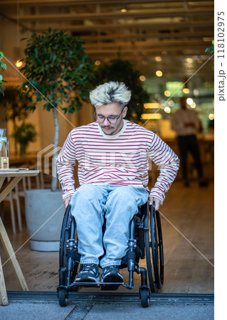 Serious focused man with disability in wheelchair drives out of cafe, trying to cross door threshold 118102975