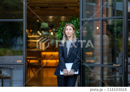 Thoughtful confident woman with laptop in hands standing at entrance of cafe in morning pondering. Thoughtful confident woman with laptop in hands standing at entrance of cafe in morning pondering. 118103028