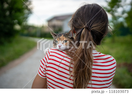 Rear view of woman back, girl holding serious cat, face peeking over shoulder with harsh expression 118103073