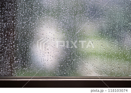 Rain droplets slide down windowpane, sunlight glimmers faintly outside. Overcast weather, depression 118103074